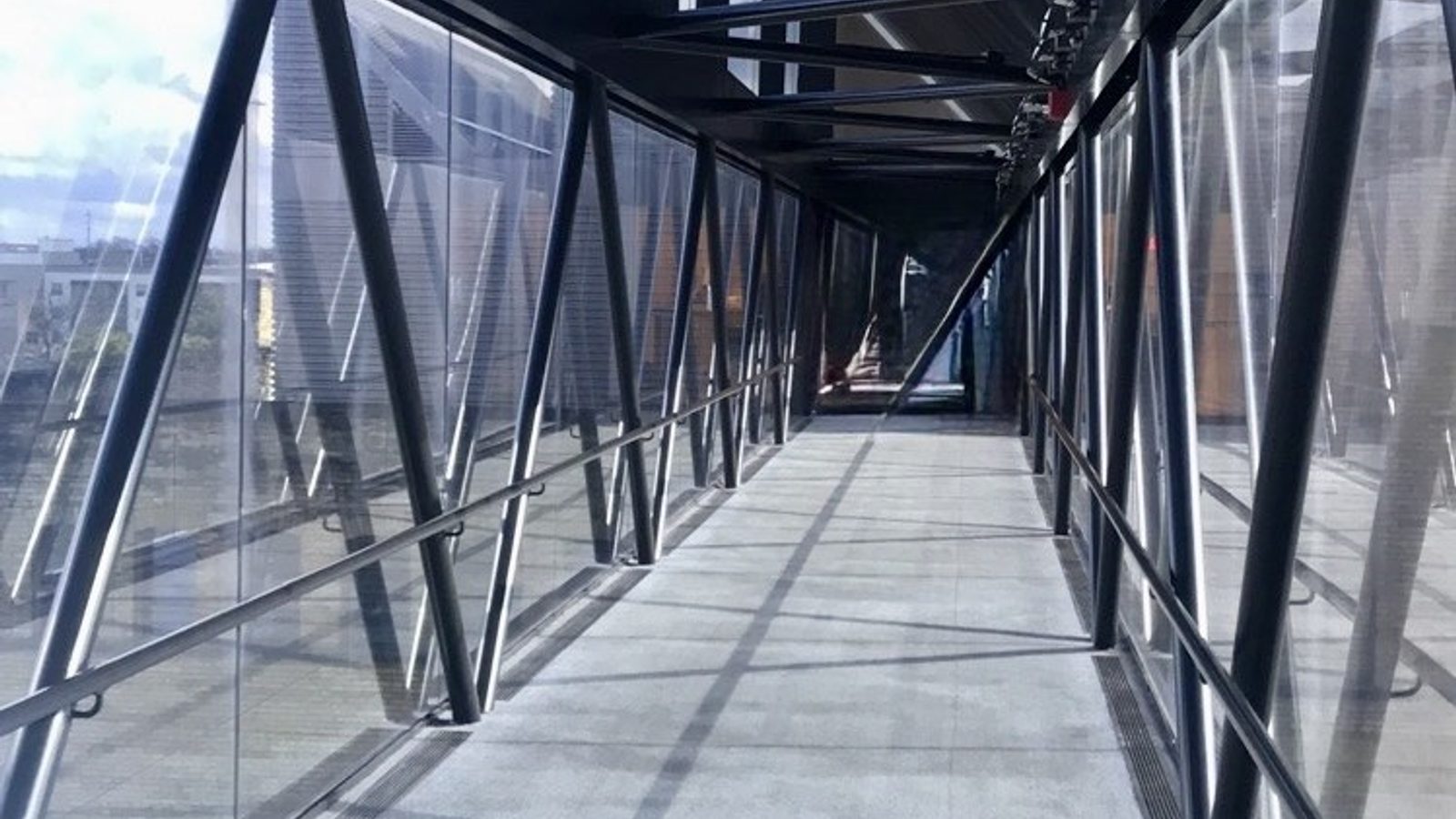 Architectural walkway with exposed steel beams and floor-to-ceiling glass, perspective lines converging toward a distant entrance — visual metaphor for operational infrastructure.