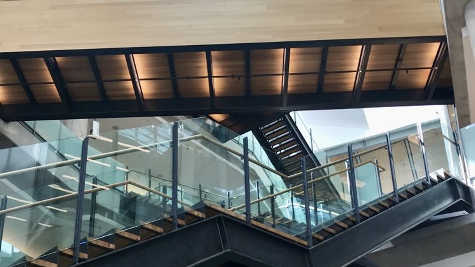 Interior of the Austin Central Library viewed from below: a glass-and-wood pedestrian bridge spans overhead on exposed metal beams, with layered floors and glass railings on multiple levels.